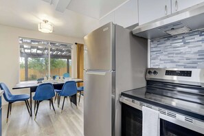 Una cocina moderna con un refrigerador de acero inoxidable, un horno empotrado y una zona de comedor con sillas azules y una mesa.