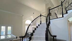 Une pièce spacieuse avec un magnifique escalier, une table de billard et une grande fenêtre.