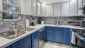 Een moderne keuken met blauwe kastjes, roestvrijstalen apparatuur en een betegelde achterwand.