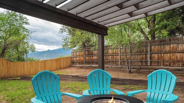 Een overdekt terras met twee turquoise Adirondack-stoelen en een zwarte vuurkorf.