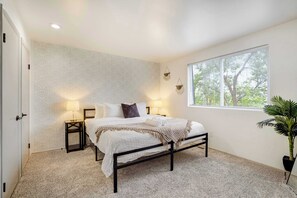 Un dormitorio con cama, lámparas de noche, una ventana con persianas, una planta y un papel tapiz estampado.
