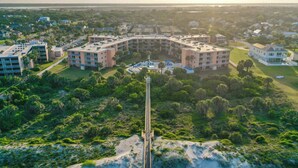 An aerial view of a resort with a central building surrounded by lush greenery and a sandy beach. - Gone Coastal l Steps to Beach l Sleeps 6 (St. Augustine)