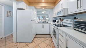A modern kitchen with white cabinets, a refrigerator, microwave, oven, and a toaster. - Gone Coastal l Steps to Beach l Sleeps 6 (St. Augustine)