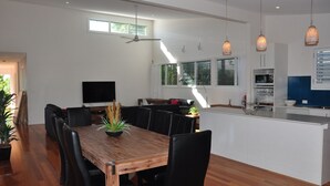 A modern kitchen with a central island, a dining area with a wooden table, and a TV mounted on the wall.