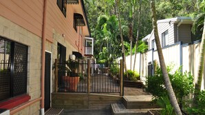 Un quartier résidentiel doté d’une entrée sécurisée par un portail, d’un petit escalier en bois et d’une variété de plantes et d’arbres.