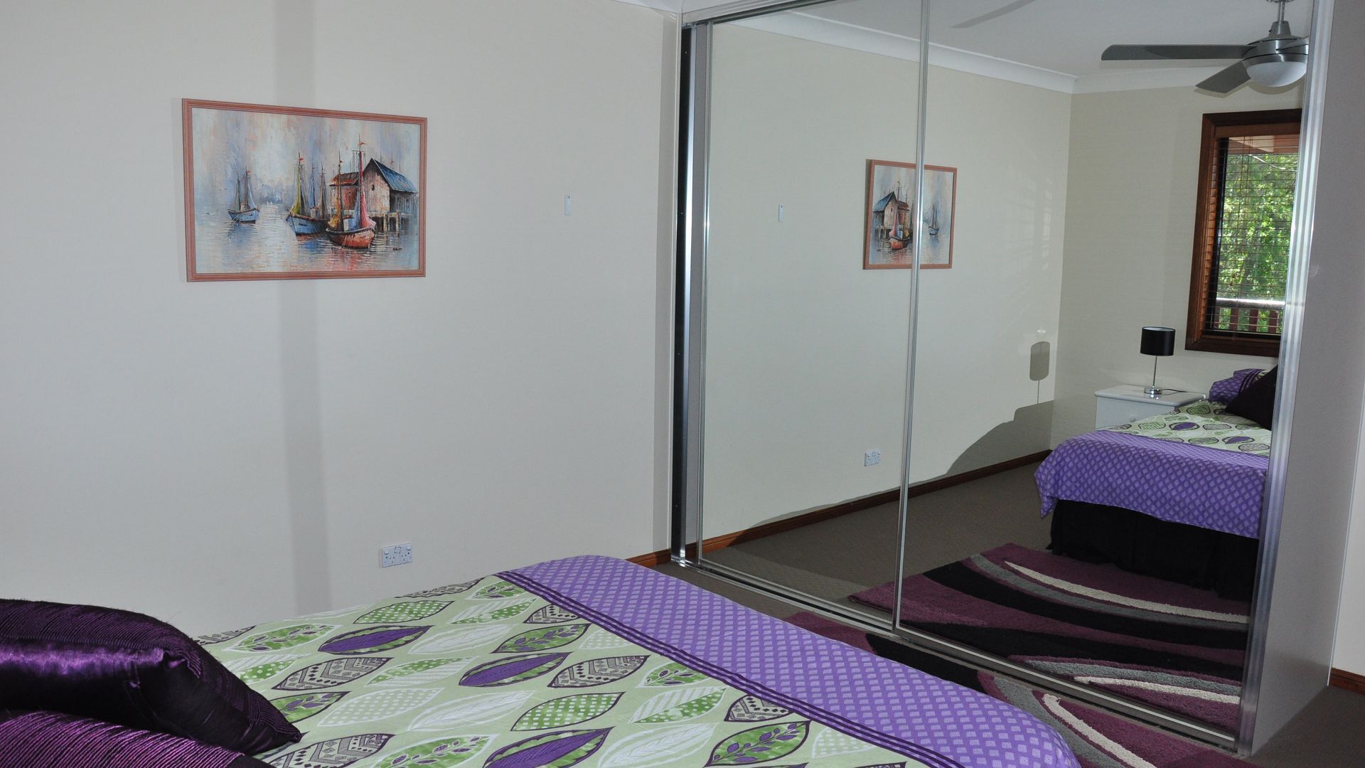 A bedroom with a bed, a mirror, and two paintings on the wall.