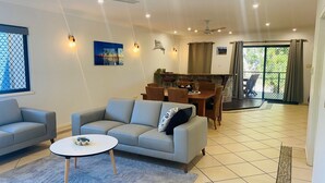Un salon moderne avec un canapé gris, une petite table ronde et un coin repas doté de chaises en osier.