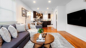 A modern living room with a dark sofa, a round coffee table, and a flat-screen TV mounted on the wall.