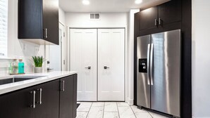 A modern kitchen with dark cabinetry, a stainless steel refrigerator, and a double door closet.
