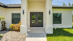 A modern house with a double door entrance, a small porch, and a well-maintained lawn. - Golf Days & Beach Fun: Port Charlotte Home w/ Yard (Port Charlotte)