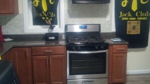 A kitchen with wooden cabinets, a stainless steel stove, and two black wall hangings with yellow text. - 3 bedroom with free parking (Schenectady)