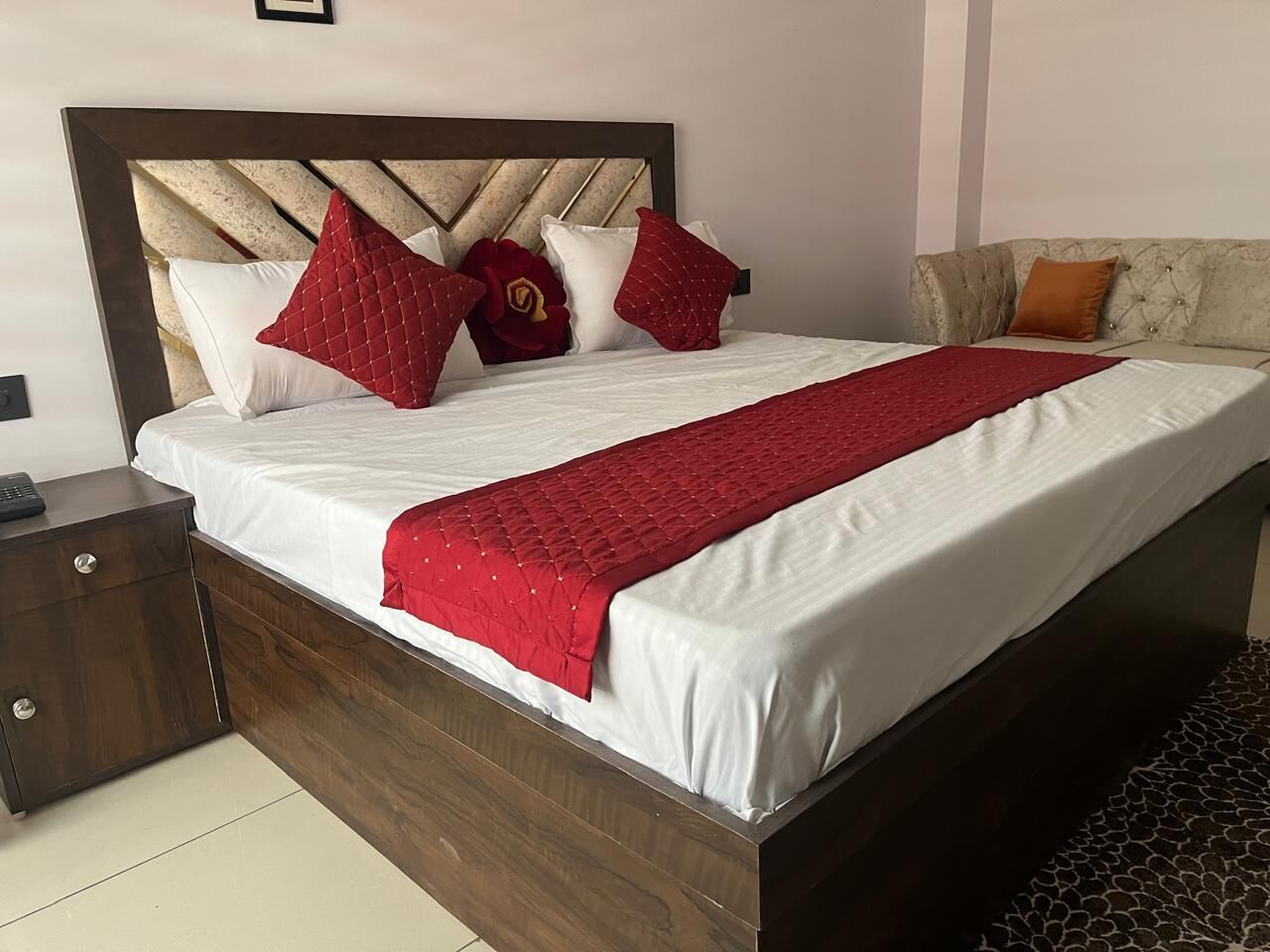 A neatly made bed with a wooden headboard, a red quilted throw, and several pillows.