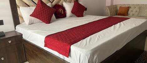 A neatly made bed with a wooden headboard, a red quilted throw, and several pillows.