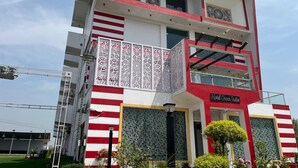 A two-story building with a red and white color scheme, featuring a balcony with intricate white latticework, and a sign that reads "Hotel Green India."