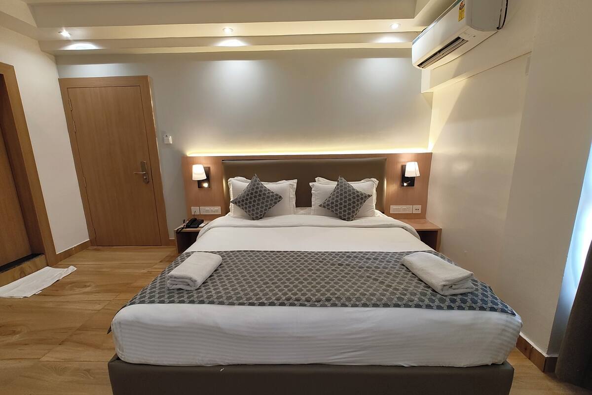 Une chambre d’hôtel avec un grand lit, deux tables de chevet avec des lampes, un climatiseur mural et une porte en bois.