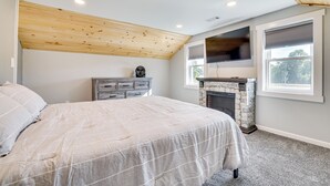 Een slaapkamer met een bed, een dressoir, een stenen openhaard en een raam met jaloezieën.