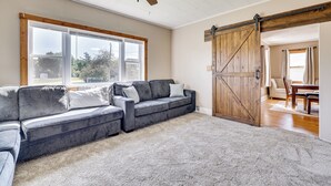 Een woonkamer met een hoekbank, een plafondventilator, een groot raam en een deur in boerderijstijl.