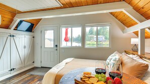Quarto com cama, bandeja de café da manhã com lanches e bebidas, televisão no teto e vista para o exterior.