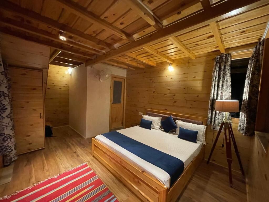 A wooden cabin bedroom with a bed, a red and white striped rug, and a wooden ceiling.
