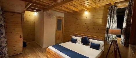A wooden cabin bedroom with a bed, a red and white striped rug, and a wooden ceiling.