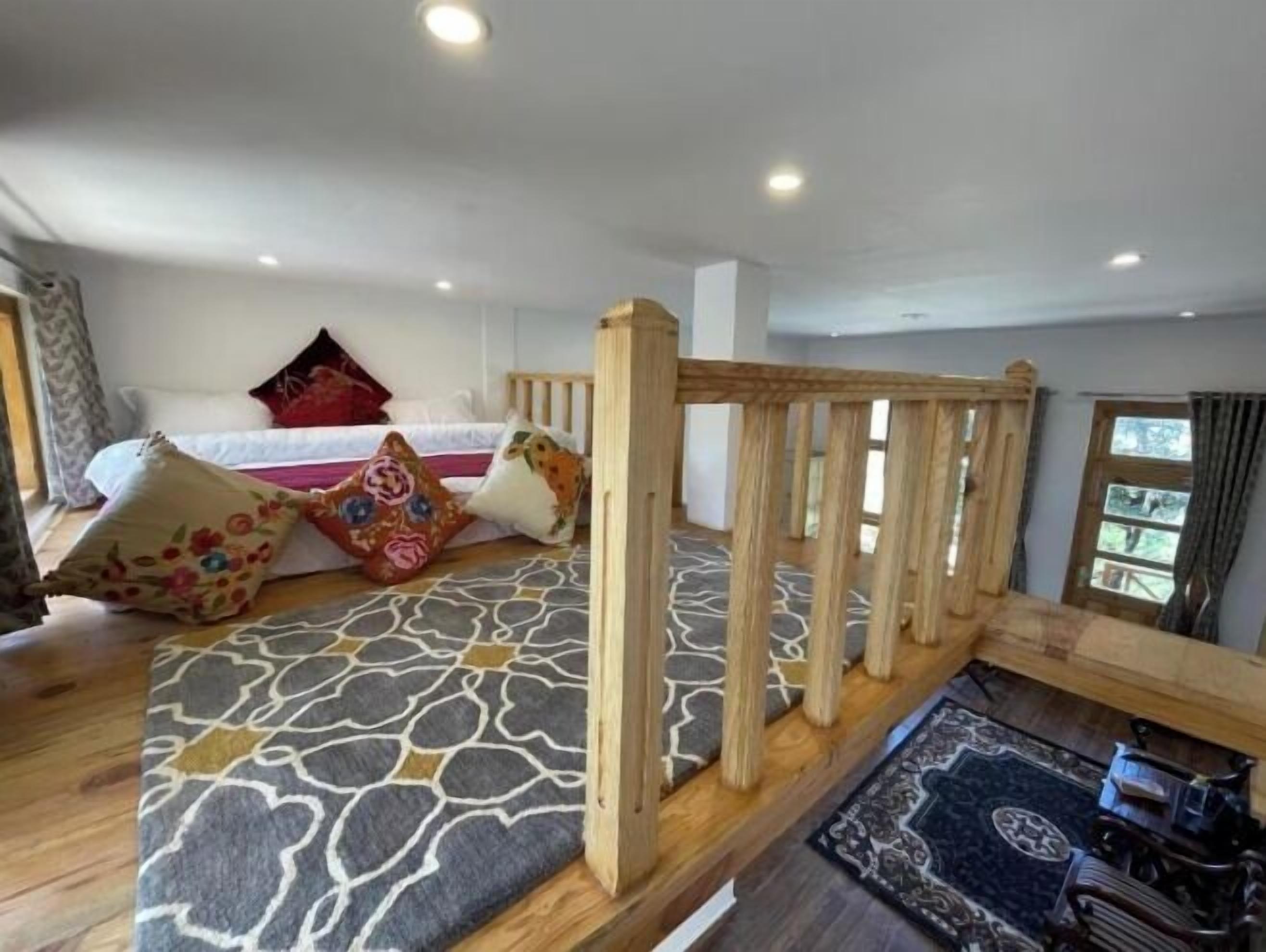 A room with a bed, colorful pillows, a wooden partition, and a patterned rug.