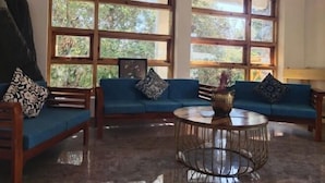 A room with a blue sofa set, a round coffee table, and large windows with a view of greenery. - Bagar Trails  (Kosiyakutoli)