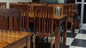 A dining area with wooden tables and chairs, a ceiling fan, and a checkered floor pattern. - Hotel Blue Diamond (Shri Madhopur)