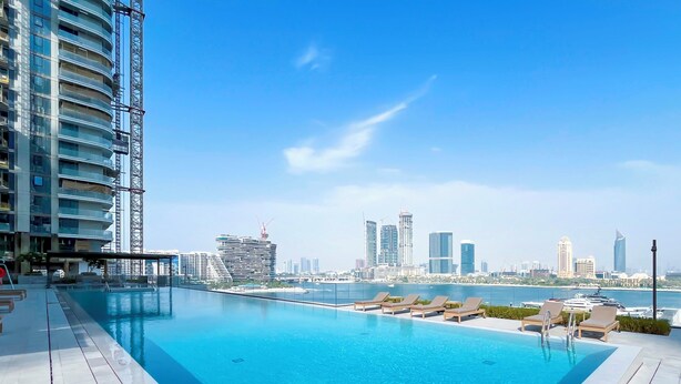 Ein Infinity-Pool auf dem Dach mit Blick auf die Stadtlandschaft, Liegestühle und ein Hochhaus im Hintergrund.