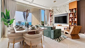 A modern living room with a dining area, large windows, a flat-screen TV, and a wooden bookshelf. - FIRST CLASS | 4BR | Elegant Beach House Retreat (Palm)