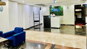 A reception area with a reception desk, a blue sofa, a ladder, and a green wall decoration. - OPO MINISTAR M180 (Gurugram)