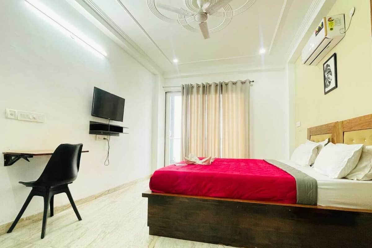 A hotel room with a bed, a desk with a chair, a television, and a ceiling fan.