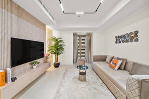 A modern living room with a flat-screen TV, a potted plant, a sofa with cushions, and a decorative wall piece. - FIRST CLASS | 2BR | Luxury Marina Bliss (Marina)