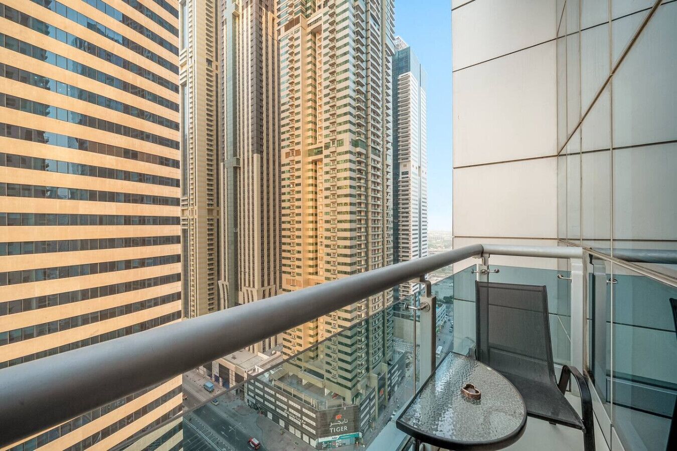 A high-rise building with a modern design, featuring a balcony with a glass railing and a small table.