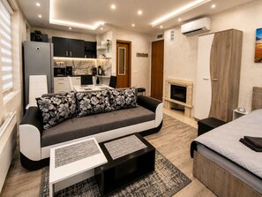 A modern living room with a sofa, a coffee table, a fireplace, and a kitchen area. - Elegant Ground-Floor Studio with Covered Terrace and Direct Access to Nature (Пампорово)