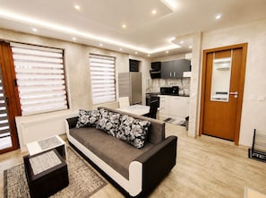 A modern living room with a sofa, a dining table, and a kitchen area with cabinets and appliances.