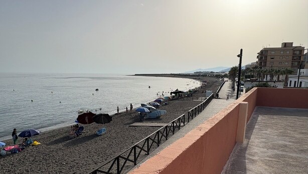 Ein Strand mit Sonnenschirmen, Liegestühlen und einer Promenade.