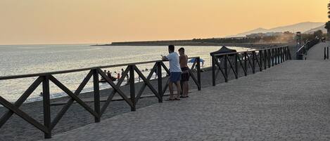 Een verharde promenade met een balustrade, met uitzicht op een wateroppervlak, waar mensen staan en lopen.