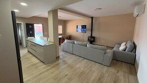 Ein modernes Wohnzimmer mit Küchenbereich, einem großen grauen Sofa, einem flachbildfernseher an der Wand und einem eingebauten Kamin.