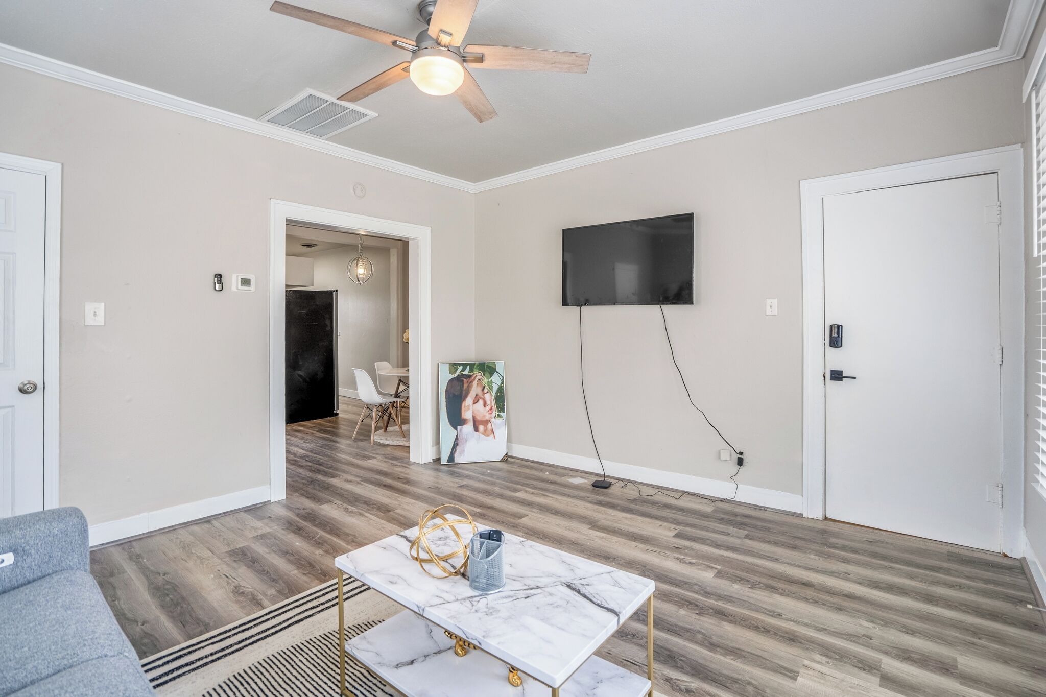 A living room with a ceiling fan, a flat-screen TV mounted on the wall, a marble coffee table, and a grey sofa.