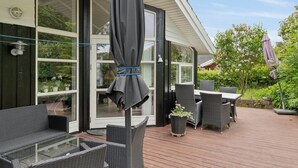 Une terrasse avec des meubles en osier, une table en verre et un parasol noir.