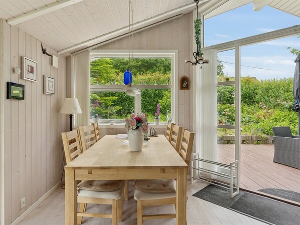 A dining area with a wooden table and chairs, a vase of flowers, and a view of greenery outside.