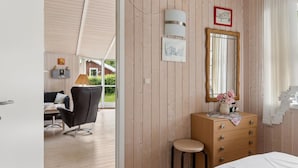 Une pièce aux murs en bois, avec un lit, une commode, un miroir et une fenêtre avec des rideaux.