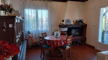 Un rincón comedor acogedor con una mesa y sillas de madera, chimenea y ventana con cortinas.