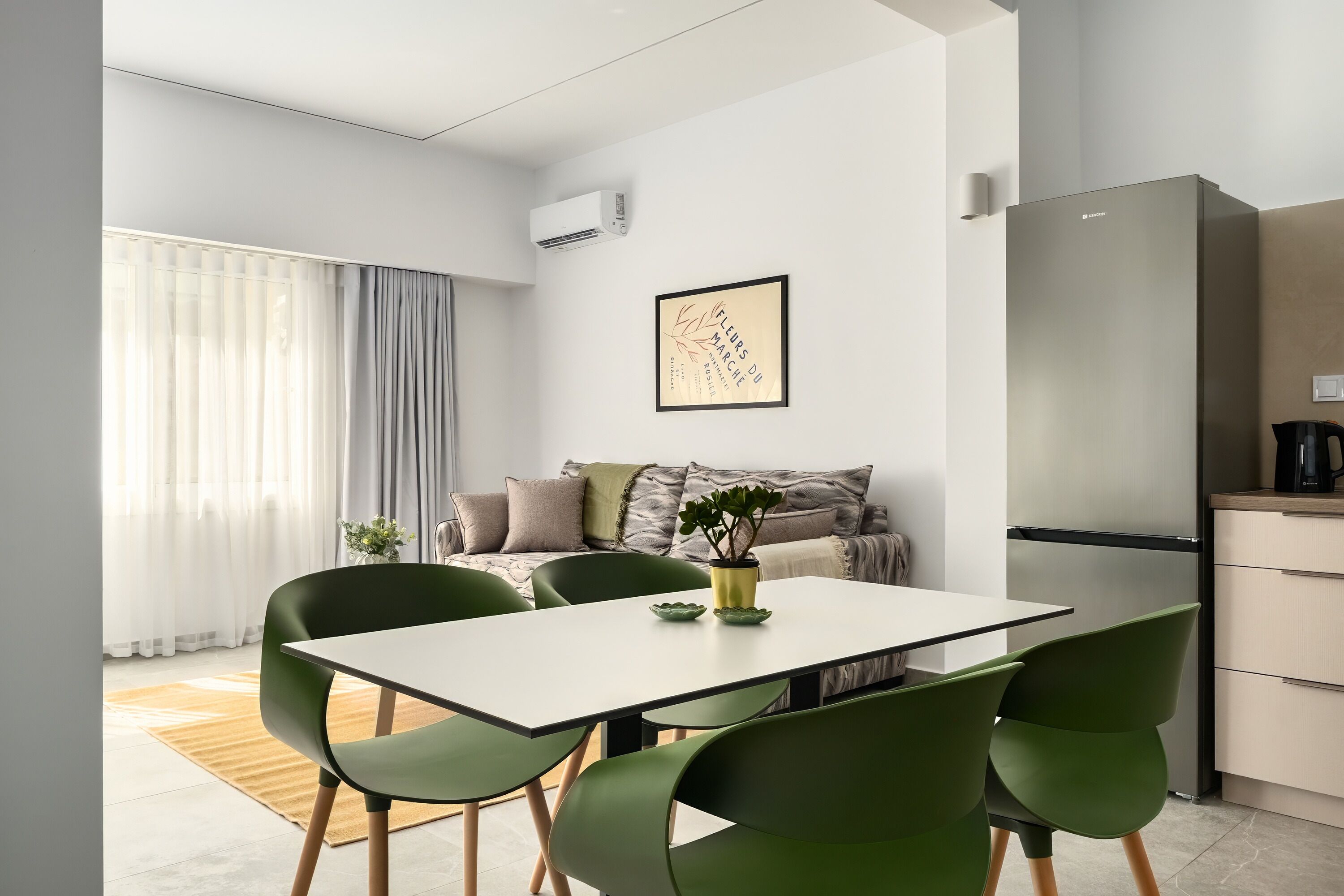A modern kitchen with a built-in refrigerator, a dining table with chairs, and a sofa in the background.