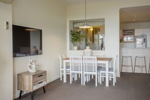 A dining area with a wooden table and white chairs, a small cabinet with drawers, and a hanging pendant light. - The Penthouse Cumberland Lorne (Lorne)