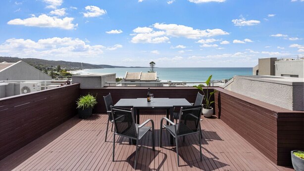 Een terras op het dak met een tafel en stoelen, met uitzicht op de kust.