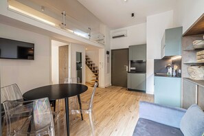 Una cocina moderna con horno empotrado, un comedor con mesa redonda y sillas, y una escalera que lleva a un nivel superior.