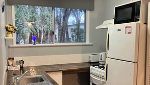 Une cuisine compacte dotée d’un plan de travail en bois, d’un évier en acier inoxydable, d’un réfrigérateur blanc, d’un four à micro-ondes et d’un four traditionnel.