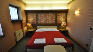 A hotel room with a large bed, two bedside lamps, a window with curtains, and a floral-patterned headboard.