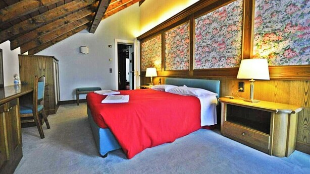 A bedroom with a large bed, wooden headboard, two bedside lamps, and a wooden desk with a chair.